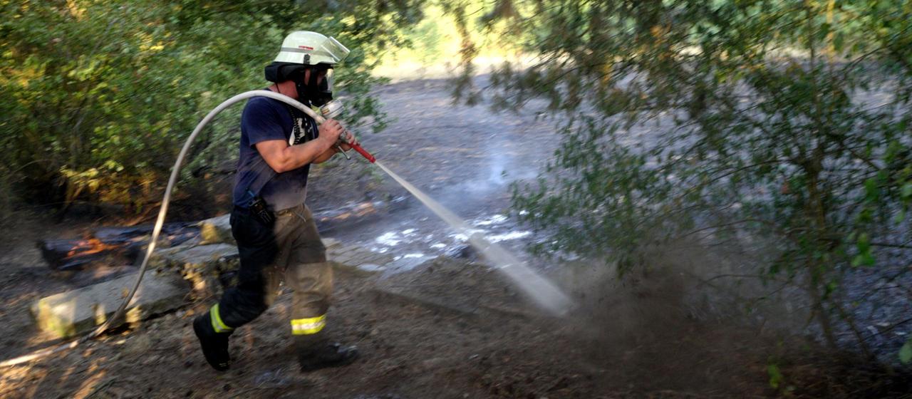  Ein Feuerwehrmann löscht einen Brand in einem Waldstück in Lingen, Niedersachsen.
