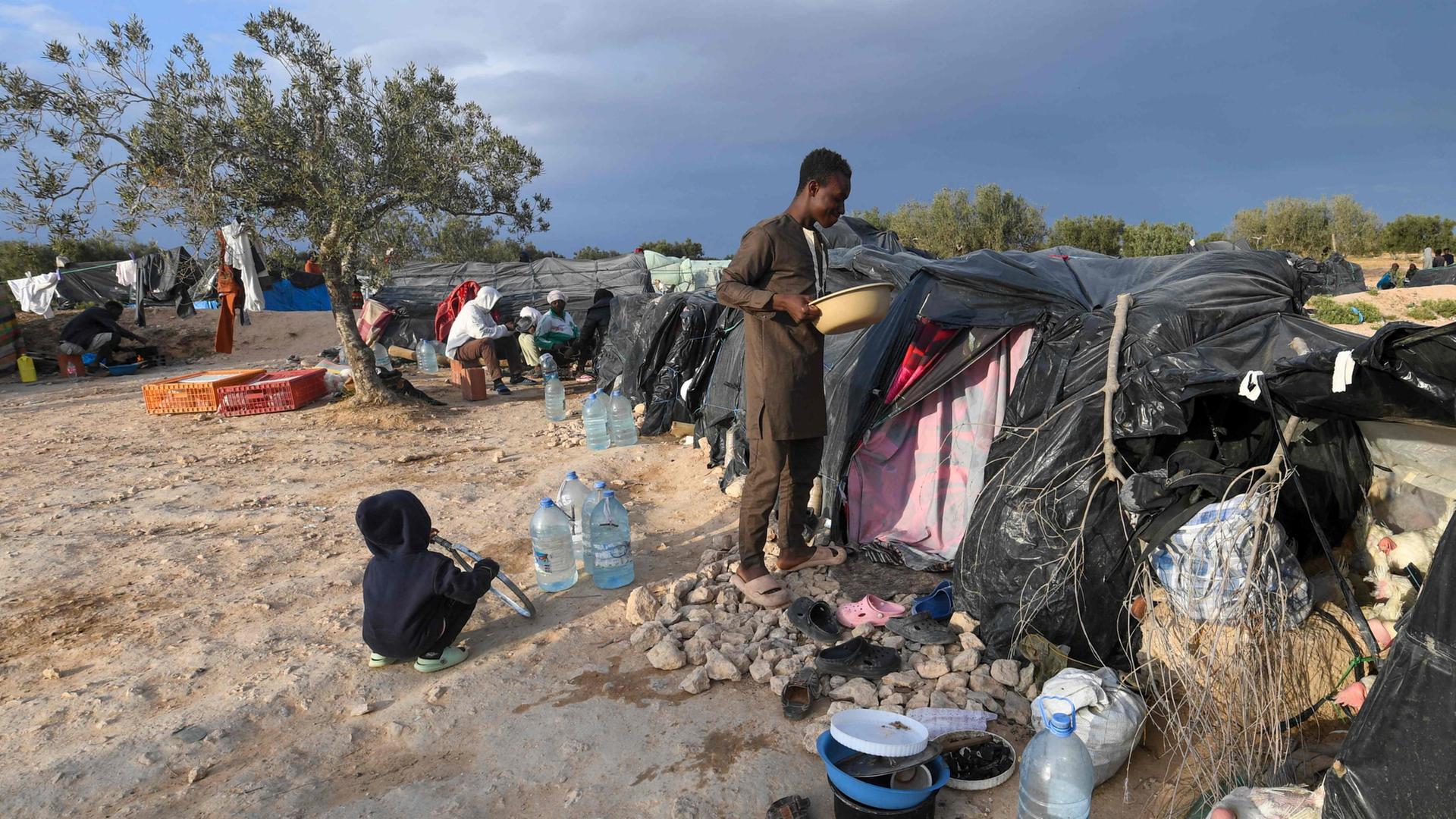 Migranten stehen vor ihren Verschlägen, die sie am Rande der tunesischen Hafenstadt Sfax errichtet haben (April 2024). | AFP