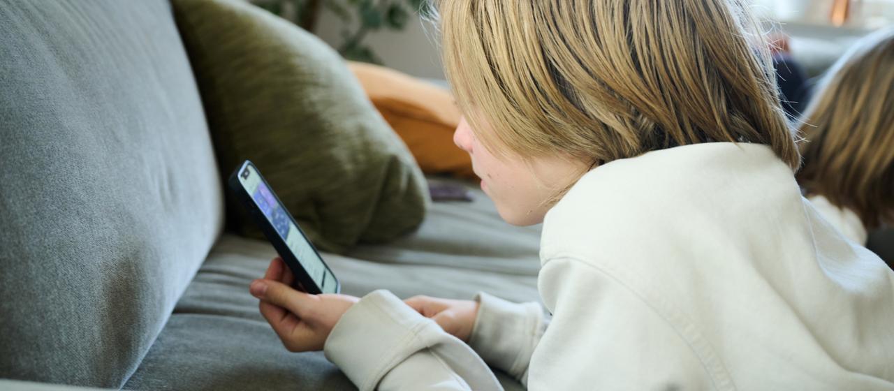 Ein Junge liegt auf einem Sofa und guckt auf sein Smartphone.