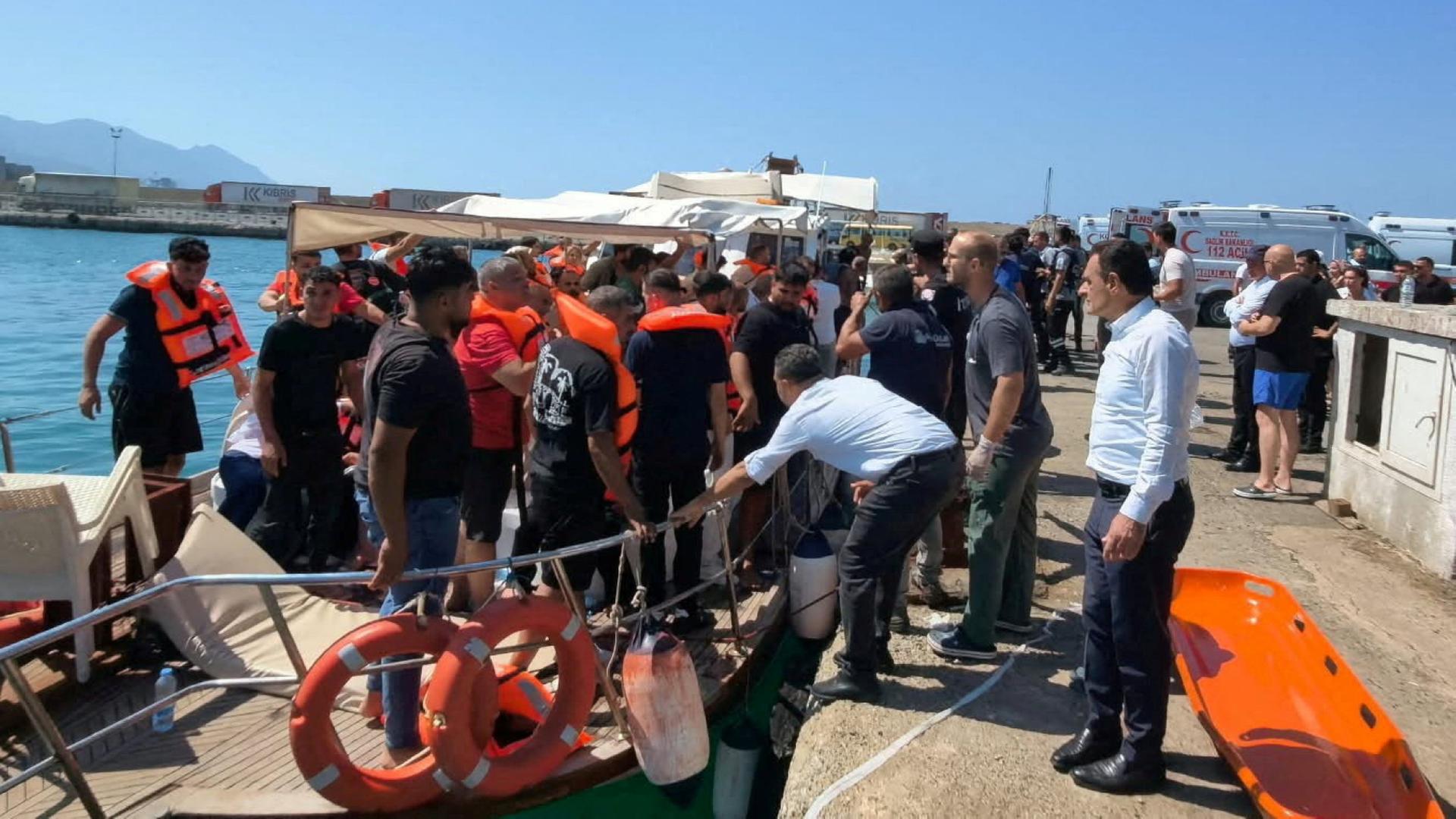 Zahlreiche Menschen zum Teil mit Rettungswesten auf und neben einem Boot. | REUTERS