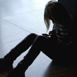 Ein Mädchen sitzt mit gesenktem Kopf allein auf dem Fußboden.