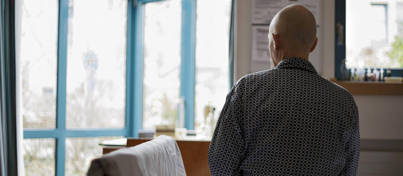 Ein Krebspatient sitzt auf einem Bett und schaut aus dem Fenster.