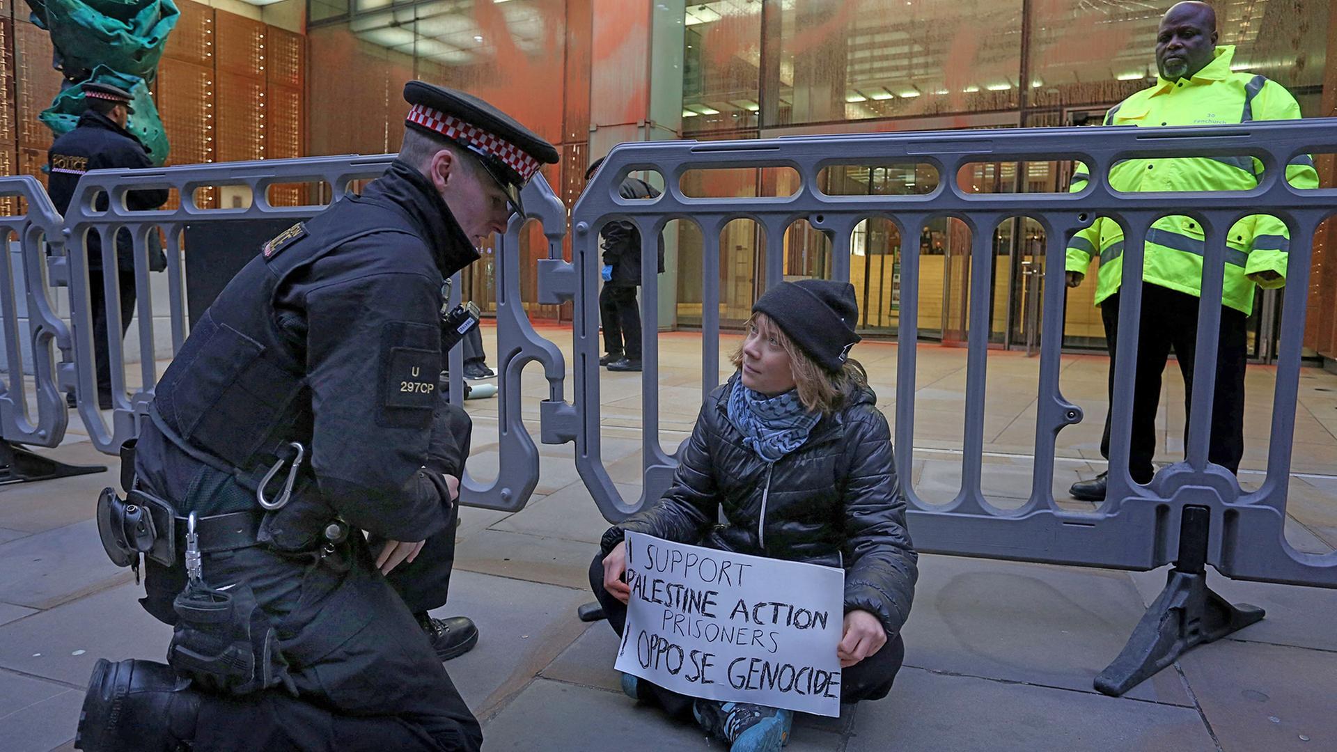 Ein Polizist kniet neben Greta Thunberg, die auf dem Boden sitzend ein Plakat in den Händen hält. | AFP