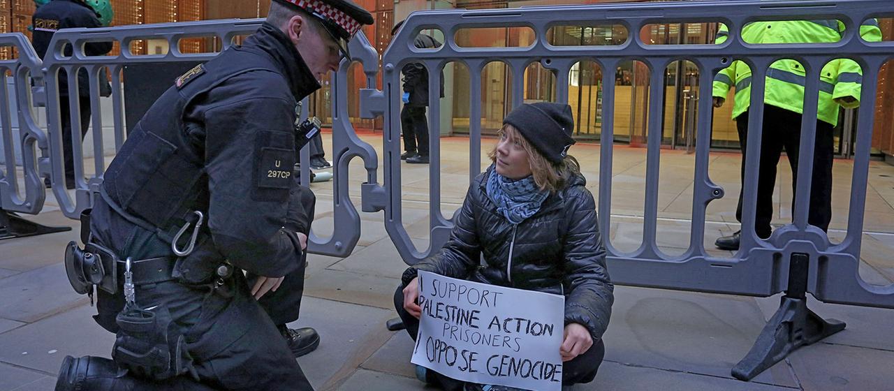 Ein Polizist kniet neben Greta Thunberg, die auf dem Boden sitzend ein Plakat in den Händen hält.