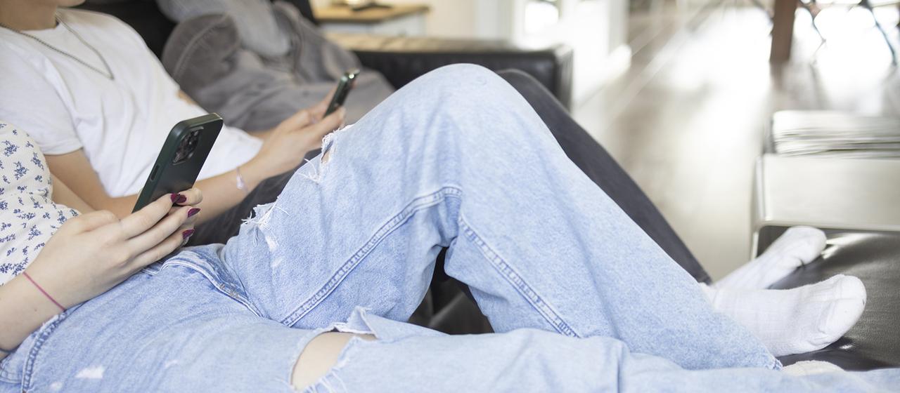 Jugendliche sitzen mit ihren Smartphones auf einem Sofa.