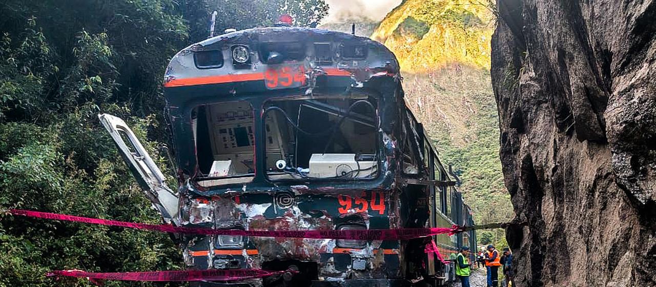 Ein demolierter schwarzer Zug steht auf einem Gleis neben einem Felsen.