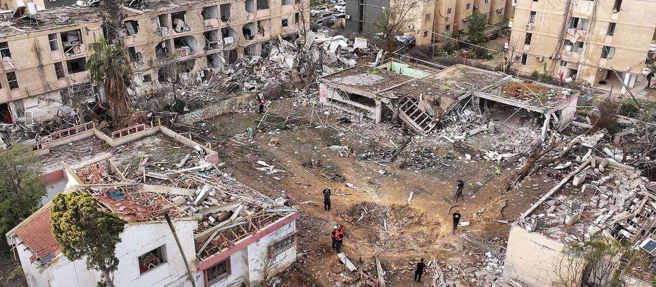 Menschen stehen in Israel in neben zerstörten Gebäuden. 