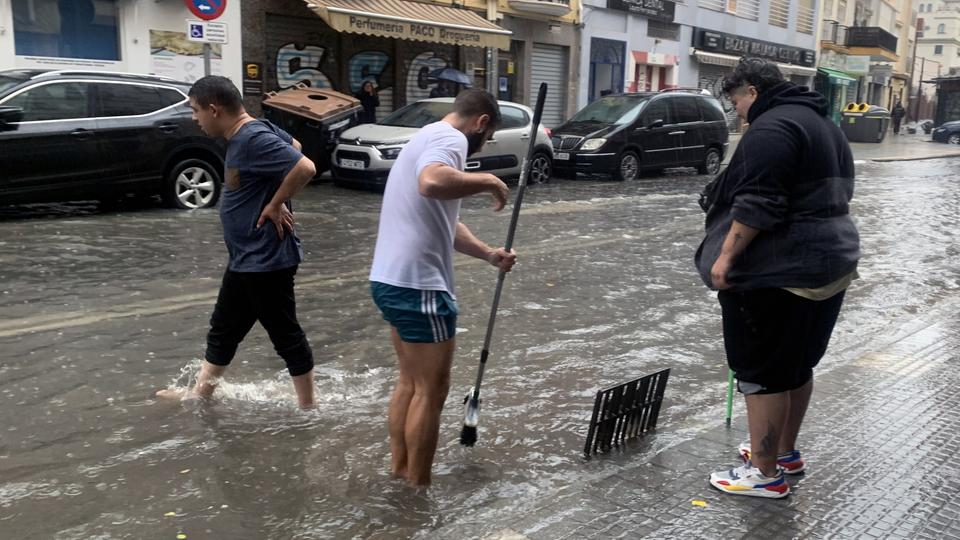Anwohner öffnen den Abwasserkanal einer überfluteten Straße in Malaga. | EPA Anwohner öffnen den Abwasserkanal einer überfluteten Straße in Malaga.