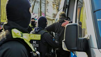 Polizisten helfen einem Mann beim Einsteigen in einen Polizeiwagen.