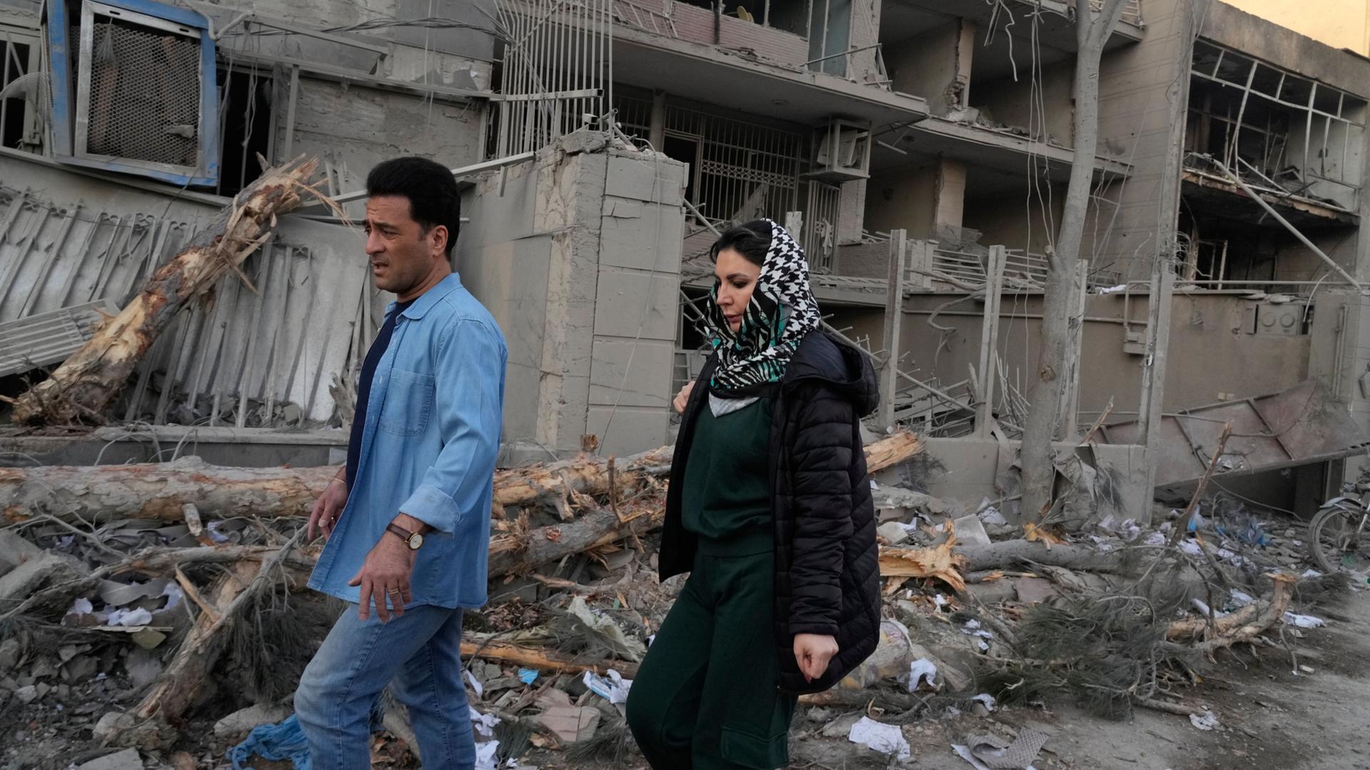 Menschen gehen an Gebäuden vorbei, die bei einem Angriff auf eine Polizeistation während der laufenden gemeinsamen US-amerikanisch-israelischen Militärangriffe in Teheran beschädigt wurden. | Vahid Salemi/AP/dpa