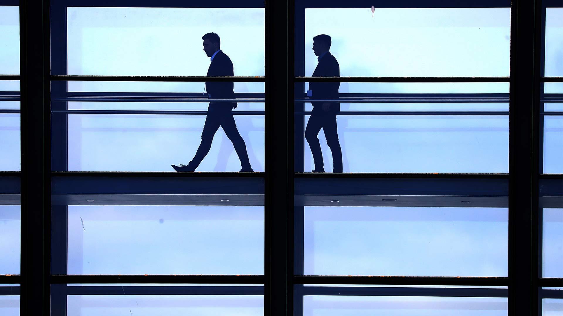 Silhouetten von zwei Männern auf dem Weg durch einen verglasten Gebäudegang. | picture alliance / empics