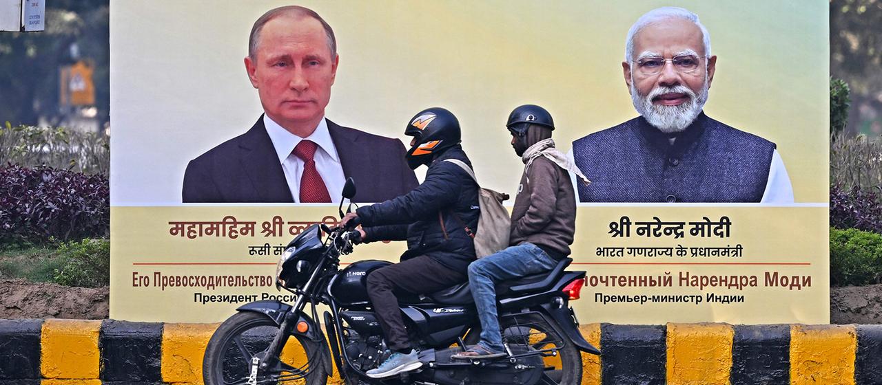 Motorradfahrer fahren an einer Plakatwand vorbei, auf der Vladimir Putin und Narendra Modi zu sehen sind.
