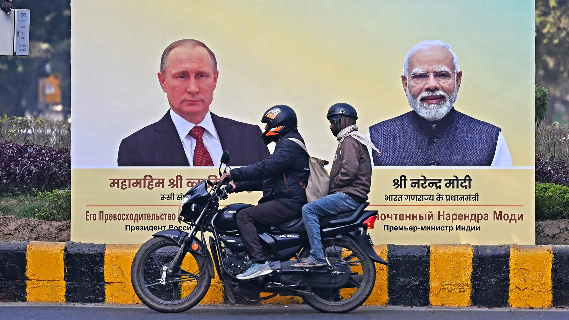 Motorradfahrer fahren an einer Plakatwand vorbei, auf der Vladimir Putin und Narendra Modi zu sehen sind. | AFP