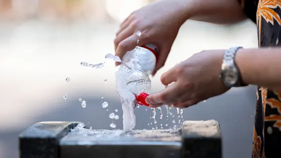 Ein Mann füllt an einem Trinkwasserbrunnen eine Flasche auf.