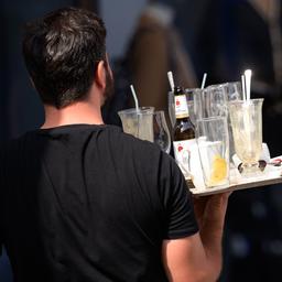 Ein Kellner trägt ein Tablett mit benutzten Gläsern und leeren Flaschen.
