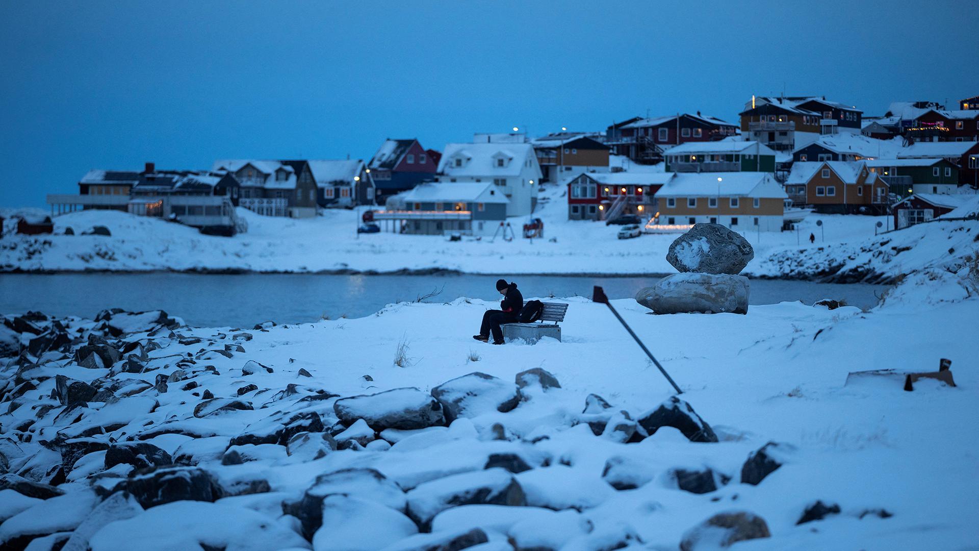 Ein Mensch sitzt im Hafen eines verschneiten Ortes auf einer Bank. | REUTERS
