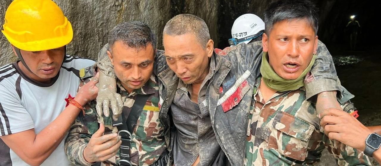 Mitglieder der nepalesischen Armee stützen einen teils mit Schlamm bedeckten Mann, den sie aus einem Tunnel tragen.