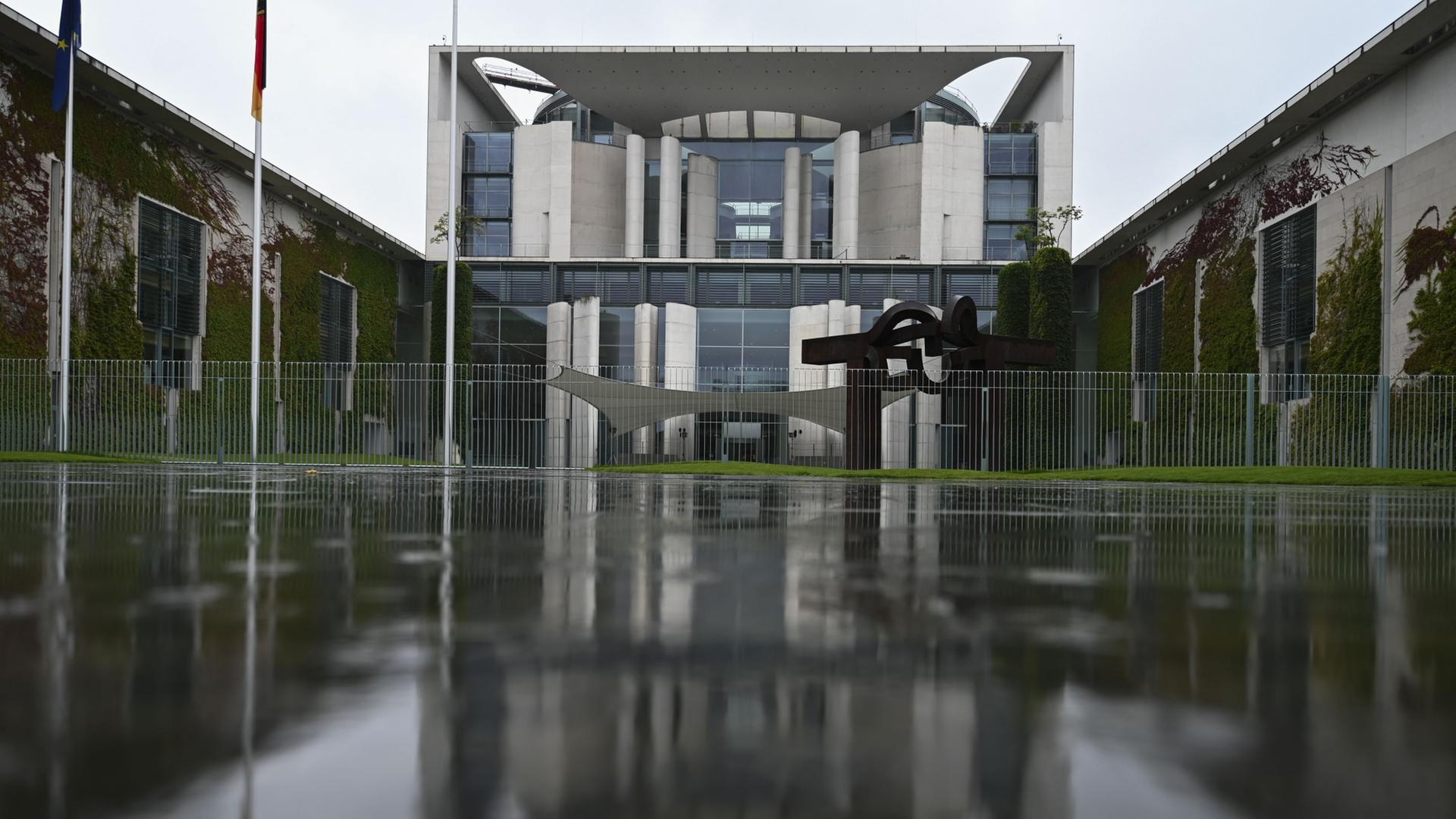 Das Kanzleramt spiegelt sich auf der regennassen Straße. | dpa