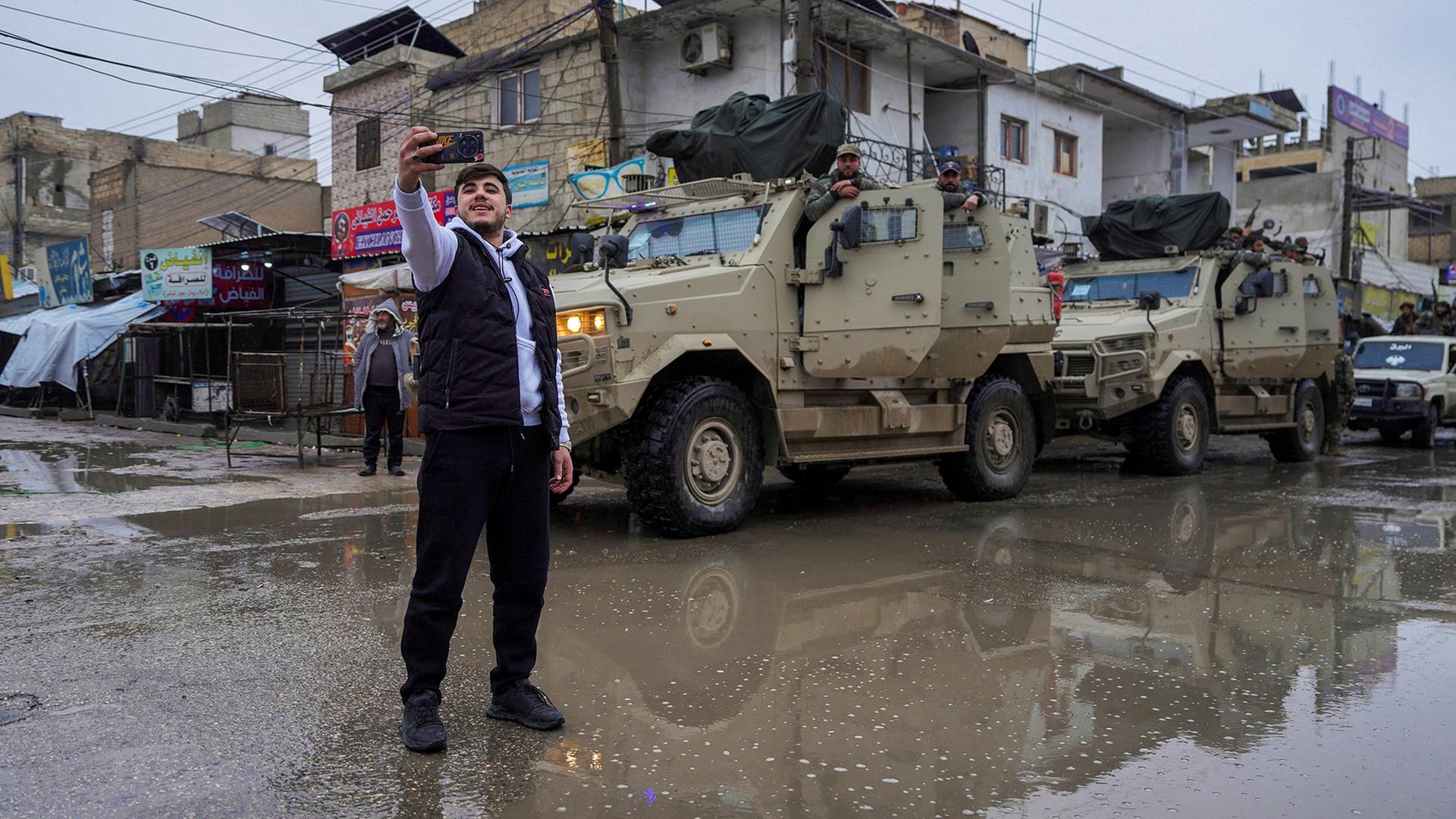 Ein Mann macht ein Selfie vor Fahrzeugen der syrischen Armee in Tabka. | REUTERS