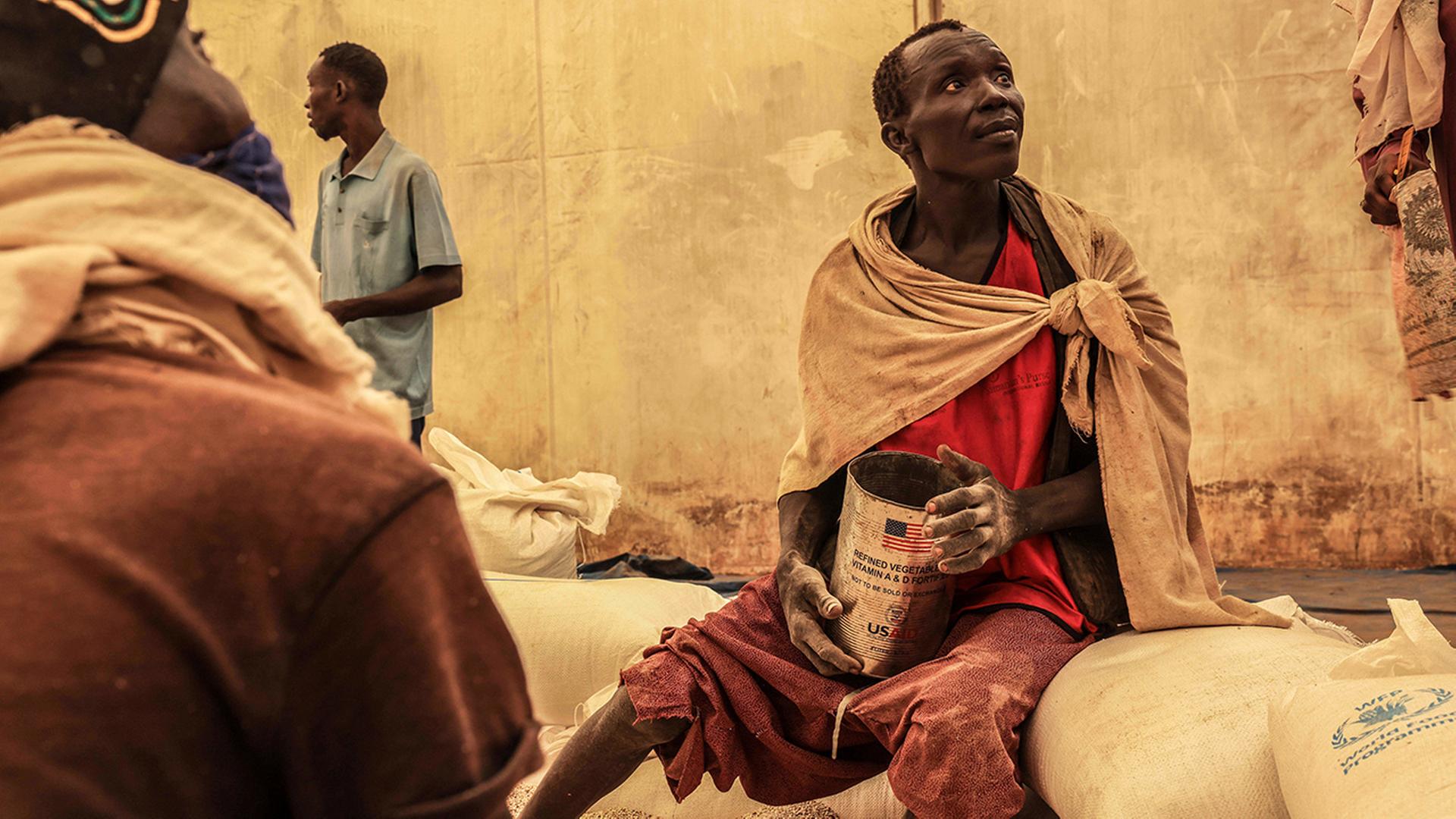 Ein Mann sitzt mit einer Dose neben Säcken von dem Welternährungsprogramm der Vereinten Nationen. | AP