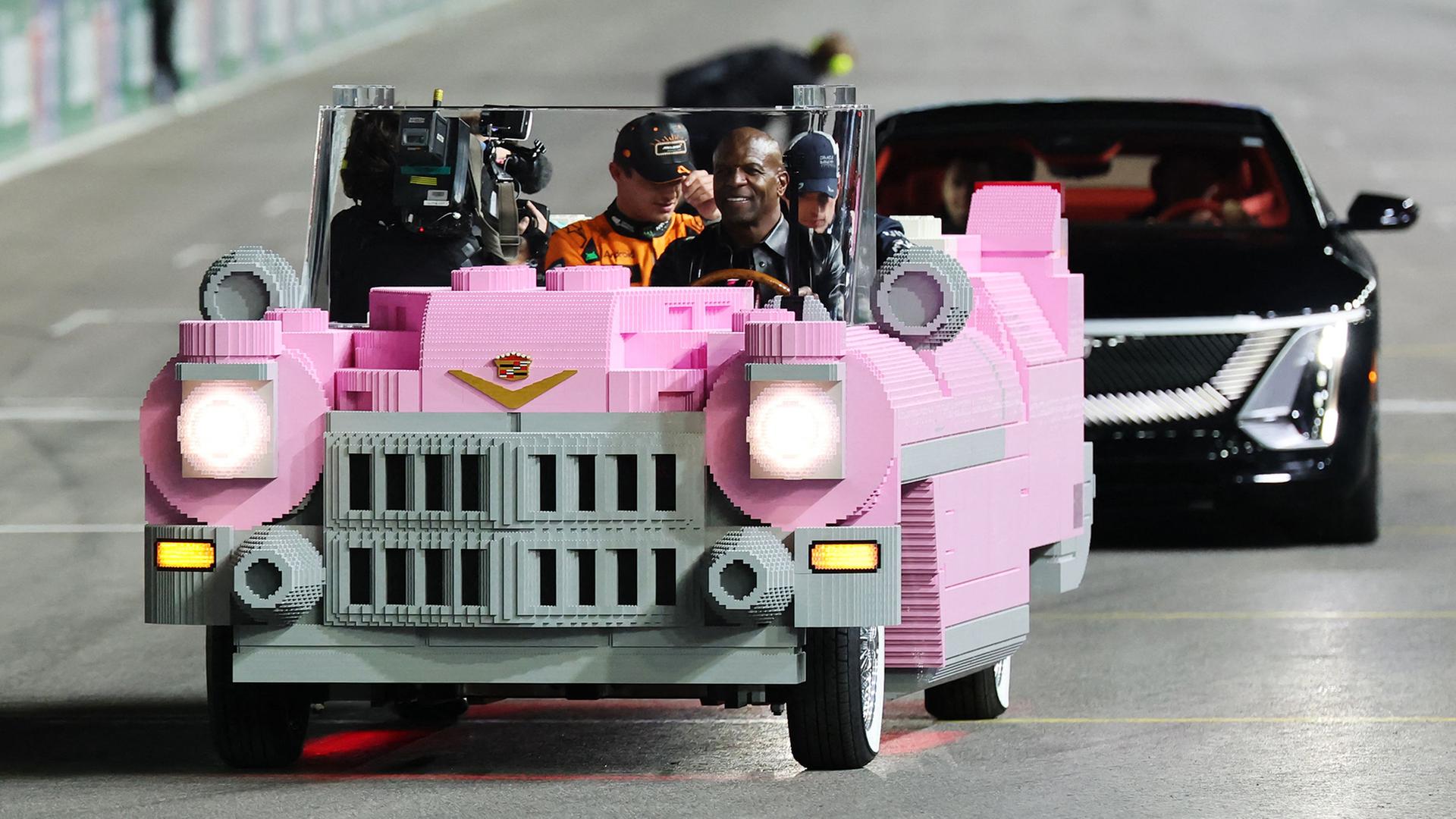 Menschen fahren in einem pinkfarbenen Lego-Cadillac über eine Autorennstrecke. | Getty Images via AFP