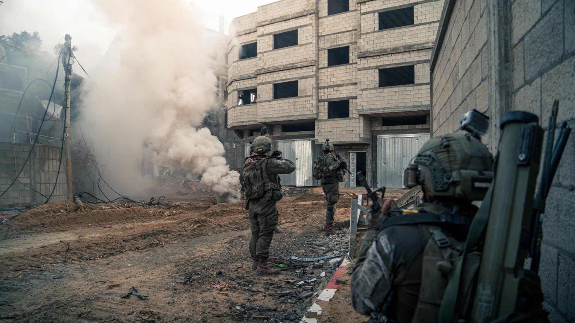 Soldaten stehen vor einem Haus, an dem Rauch aufsteigt.