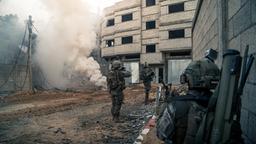 Soldaten stehen vor einem Haus, an dem Rauch aufsteigt.