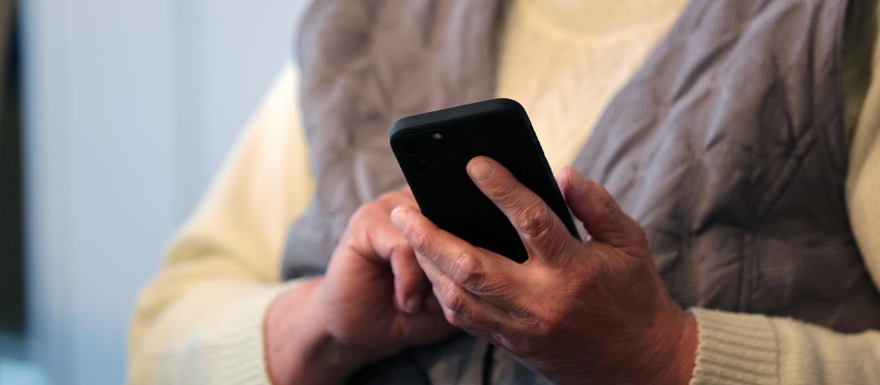 Eine Seniorin hält ein Handy in der Hand.
