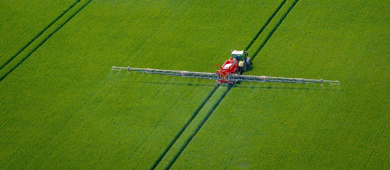 Ein Traktor zieht einen Wagen über ein Getreidefeld und verteilt Dünger.