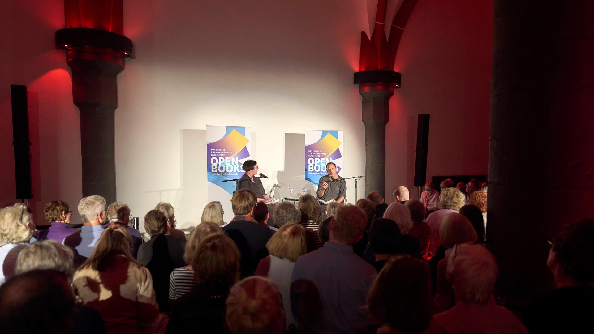Zwei Menschen auf der Bühne vor Publikum | Open Books; Alexander Paul Englert
