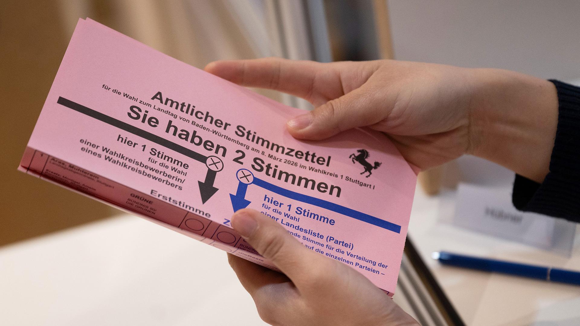 Eine Wahlhelferin zeigt im Rathaus einer Briefwählerin einen Stimmzettel zur baden-württembergischen Landtagswahl 2026. | Marijan Murat/dpa