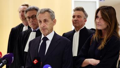 Nicolas Sarkozy steht mit seinen Anwälten und seiner Frau vor Mikrofonen im Gerichtsgebäude.