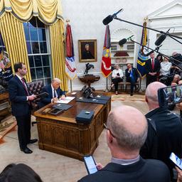 Donald Trump unterzeichnet im Oval Office vor zahlreichen Journalisten Dokumente.