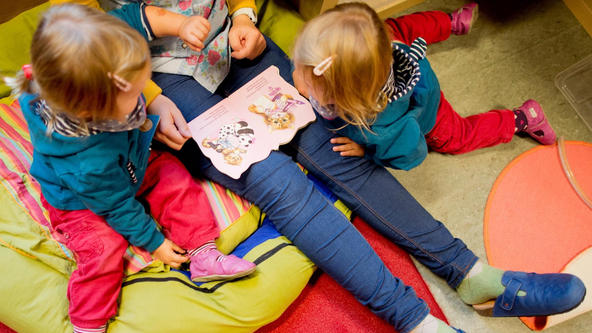  Eine Erzieherin liest mit Zwillingen ein Buch. | dpa