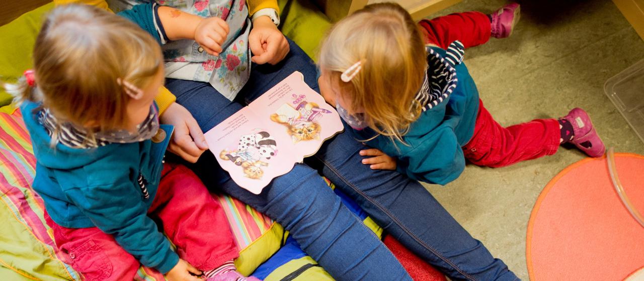  Eine Erzieherin liest mit Zwillingen ein Buch.