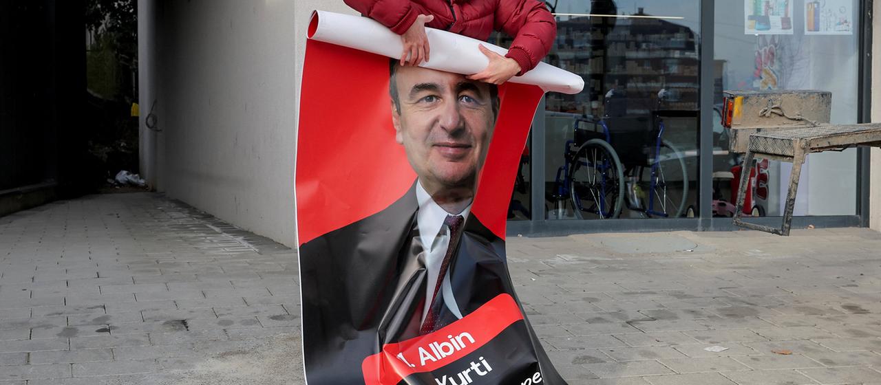 Ein Poster mit dem Bild von Albin Kurti wird eingerollt.