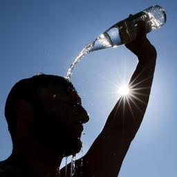 Ein Mann kühlt sich bei sommerlichen Temperaturen ab, in dem er sich eine Flasche mit Wasser über den Kopf schüttet.