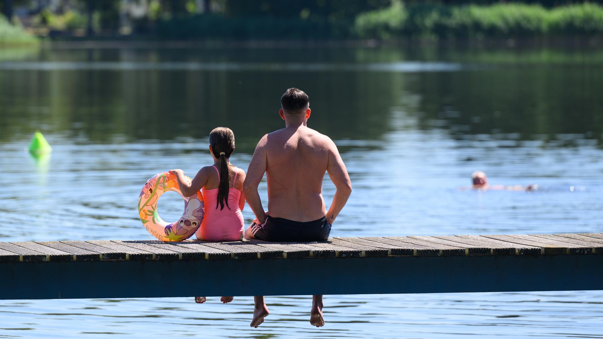 Ein Vater und seine Tochter sitzen auf einem Steg am Strandbad am Großen Müllroser See | dpa