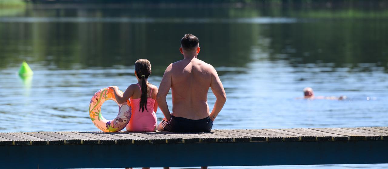 Ein Vater und seine Tochter sitzen auf einem Steg am Strandbad am Großen Müllroser See