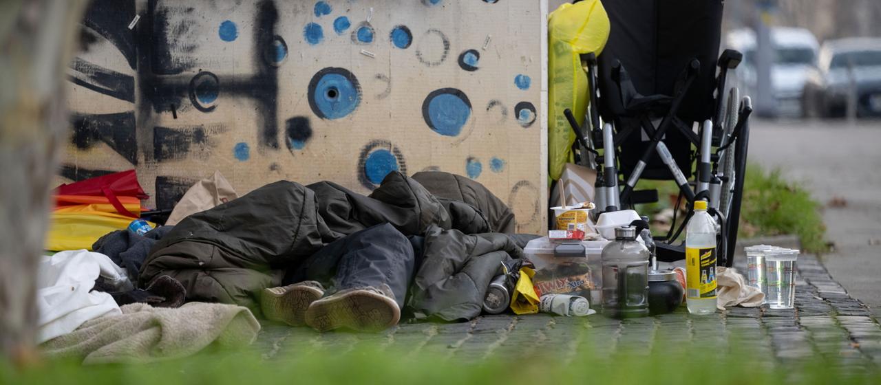 Ein Obdachloser liegt in einen Schlafsack gehüllt auf der Straße 