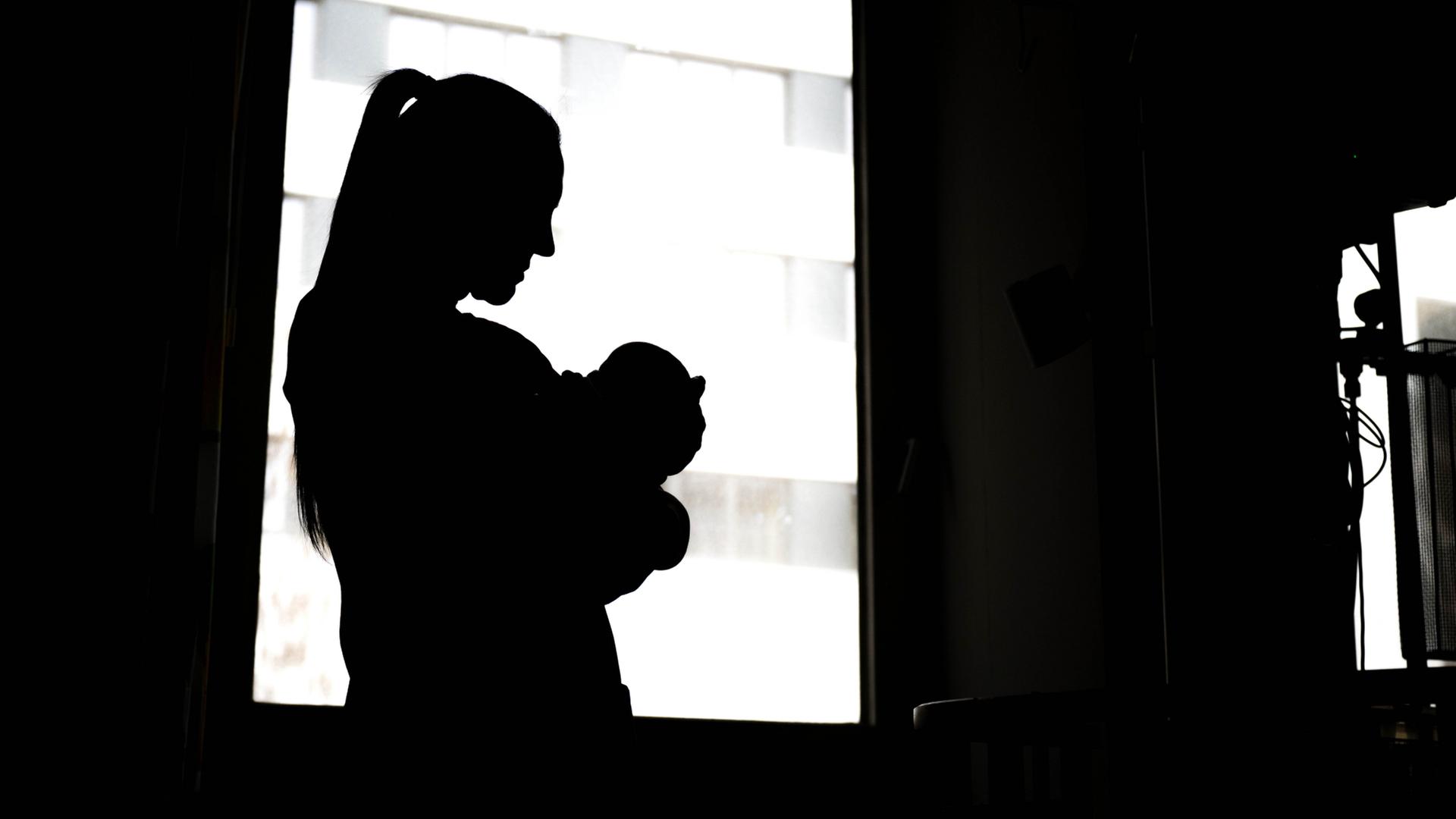 Eine Frau steht mit einem Neugeborenen am Fenster einer Klinik. | dpa