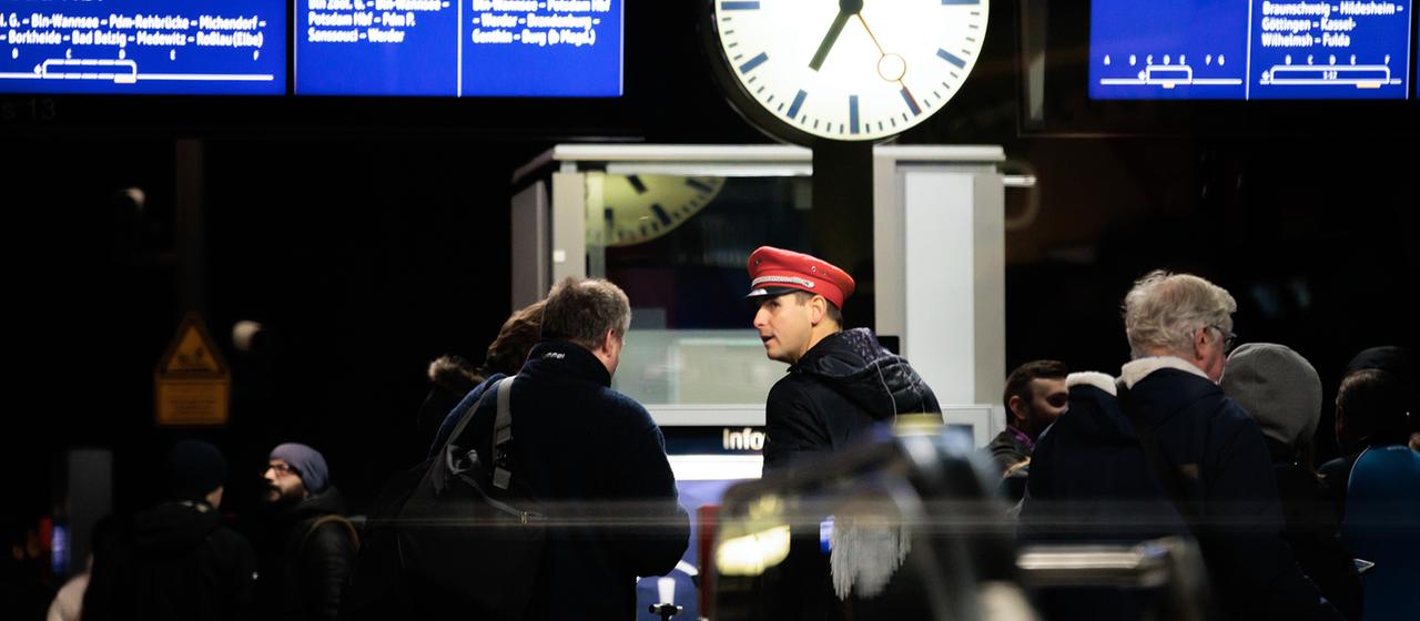 Ein Schaffner und Fahrgäste auf einem Bahngleis
