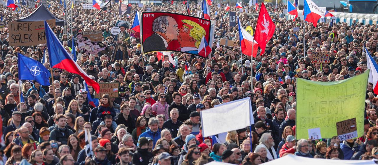 Teilnehmer einer Demonstration in Prag halten Schilder und tschechische Fahnen in die Luft.