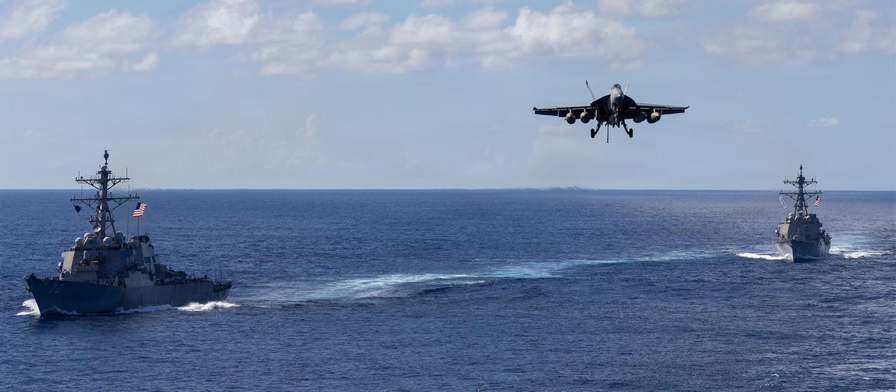 Auf diesem von der Pressestelle des Pentagons zur Verfügung gestellten Bild fahren die Lenkwaffenzerstörer der Arleigh-Burke-Klasse USS Mahan (l, DDG 72) und USS Bainbridge (DDG 96) in Formation, während ein F/A-18 Super Hornet des Carrier Air Wing Eight zur Landung auf dem Flugzeugträger USS Gerald R. Ford (CVN 78) ansetzt.