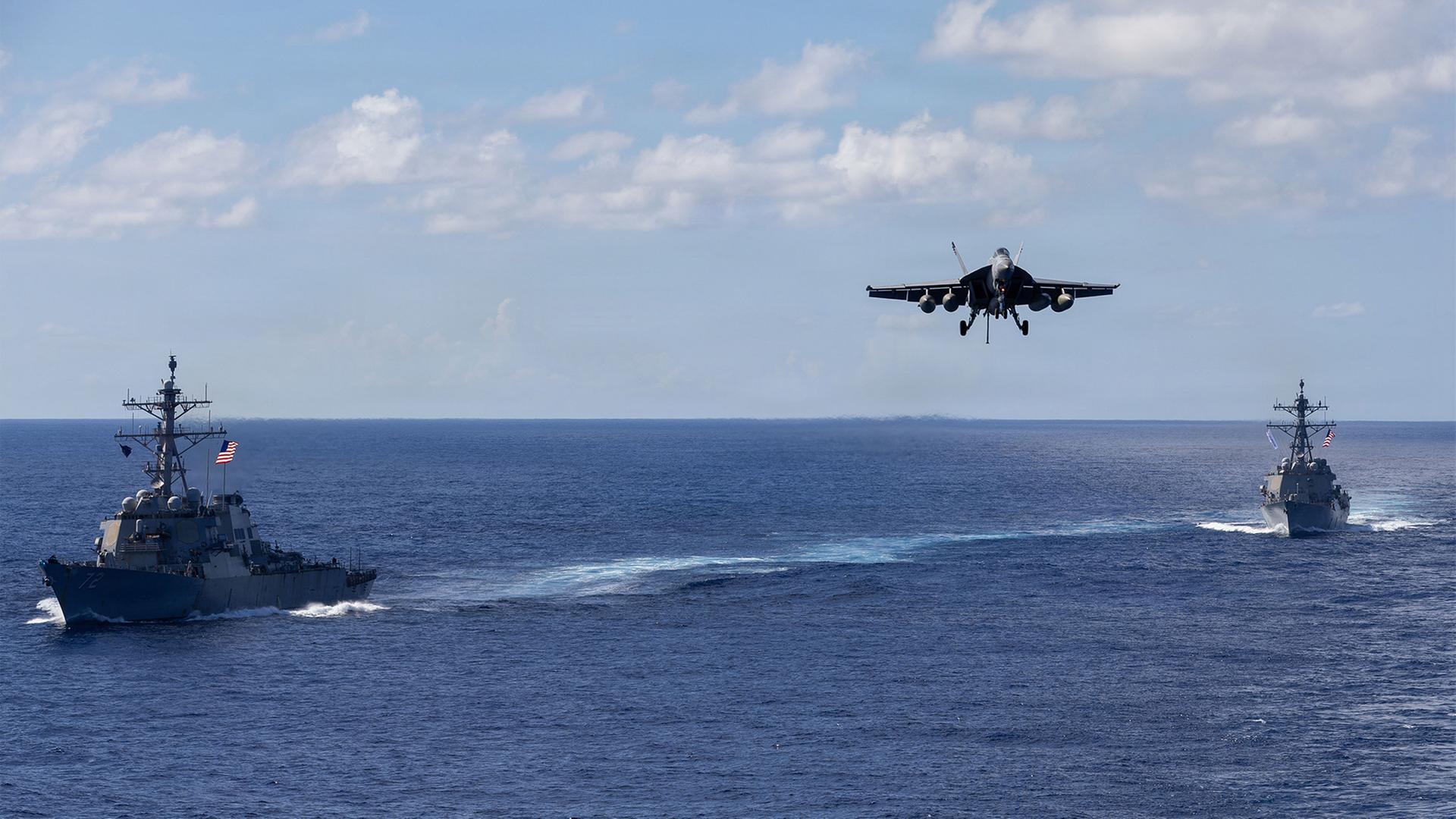 Auf diesem von der Pressestelle des Pentagons zur Verfügung gestellten Bild fahren die Lenkwaffenzerstörer der Arleigh-Burke-Klasse USS Mahan (l, DDG 72) und USS Bainbridge (DDG 96) in Formation, während ein F/A-18 Super Hornet des Carrier Air Wing Eight zur Landung auf dem Flugzeugträger USS Gerald R. Ford (CVN 78) ansetzt. | Petty Officer 2nd Class Triniti/U.S. Pentagon/dpa