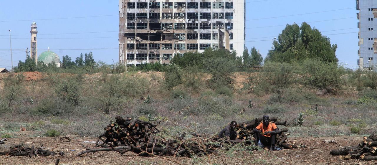 Ein Mann sitzt vor einem zerstörten Hochhaus.