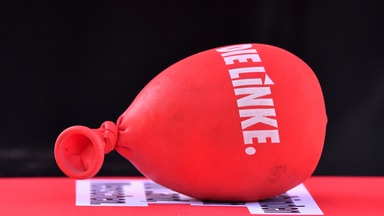 Ein mit Sand gefüllter Luftballon mit dem Aufdruck "Die Linke" liegt auf einem Tisch.