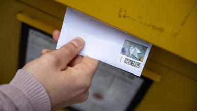Eine Frau wirft einen Standardbrief in einen Briefkasten.