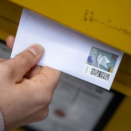 Eine Frau wirft einen Standardbrief in einen Briefkasten.