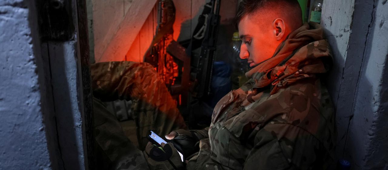 Ein ukrainischer Soldat schaut auf sein Handy in einem Lager an der Front.